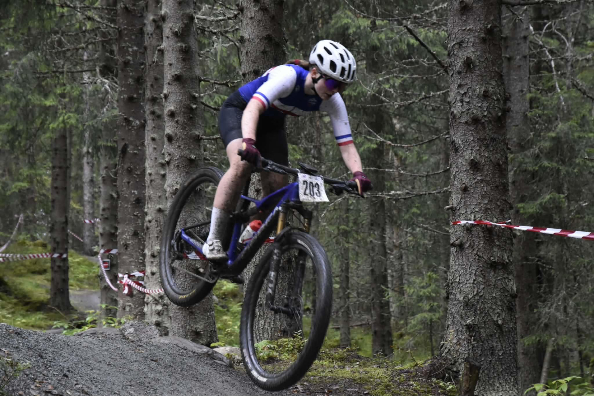 BSK-løper i klubbdress i hopp over en terskel på skogsloypa under Norgescup i terrengsykkel
